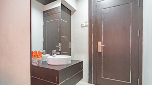 A modern bathroom with a large mirror, a sink, and a dark wooden door. - RedDoorz near Stadion Sanaman Mantikei (Palangkaraya)