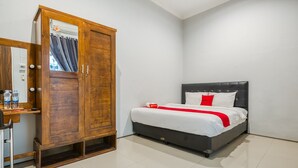 A bedroom with a bed, a wooden wardrobe, and a desk with a mirror. - RedDoorz near Surabaya Zoo (Surabaya)