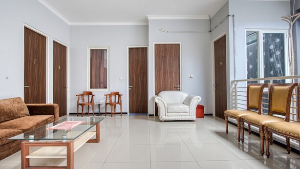 A spacious living room with a glass coffee table, a brown sofa, a white armchair, and a wooden bench. - RedDoorz near Surabaya Zoo (Surabaya)