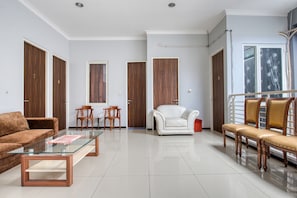 A spacious living room with a glass coffee table, a brown sofa, a white armchair, and a wooden bench. - RedDoorz near Surabaya Zoo (Surabaya)