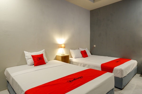 Dos camas individuales con ropa de cama blanca y detalles rojos, una mesita de noche con lámpara y una pared de acento gris.