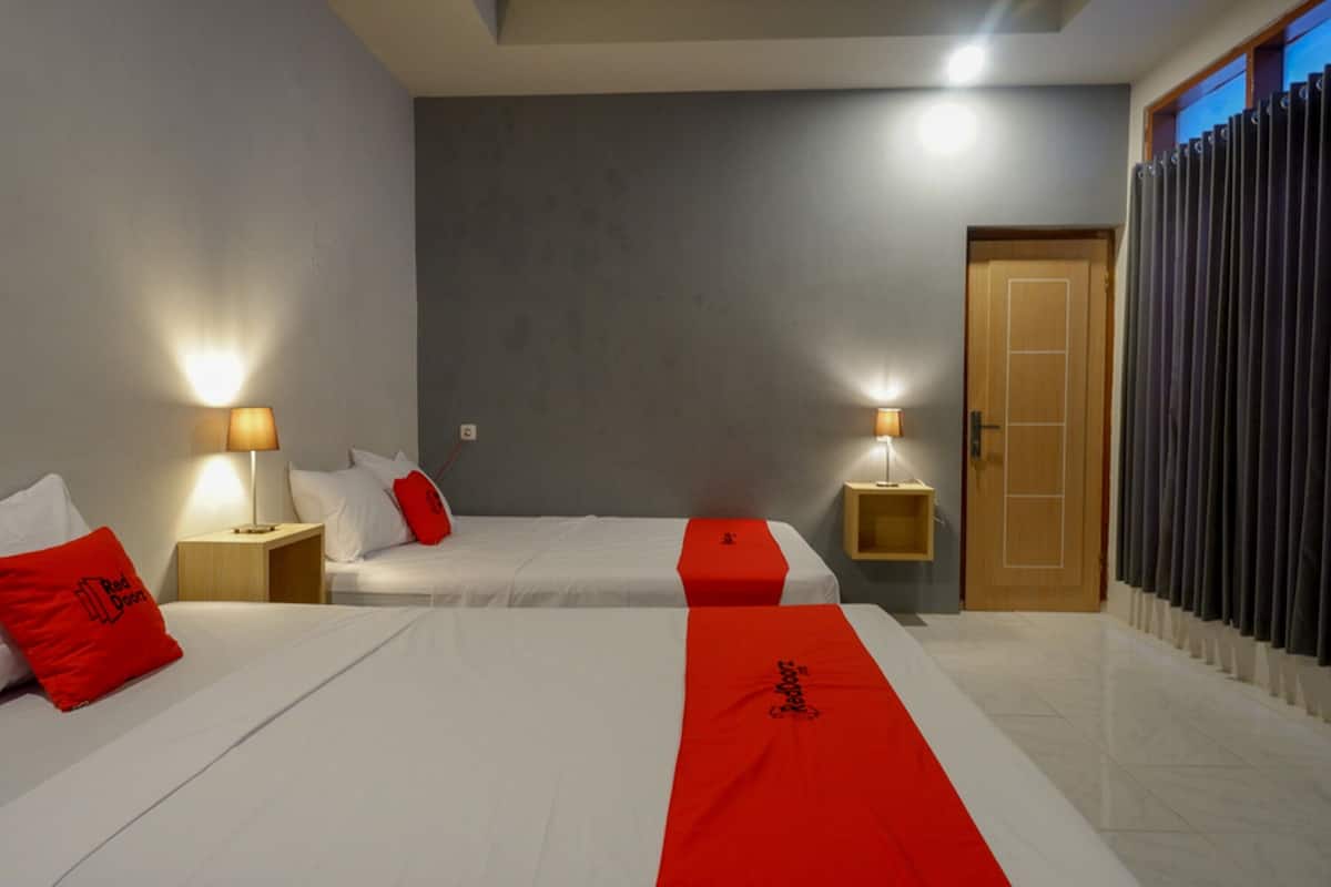 A hotel room with two beds, each with a red runner, white bedding, and a wooden nightstand with a lamp.