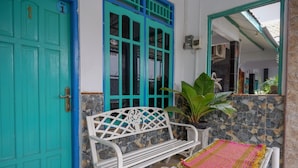 A turquoise door with a number '1' sign, a white bench, a small table with a pink and yellow woven mat, and a large green plant. - RedDoorz Syariah near Alun Alun Balai Kota Tegal (Tegal)