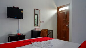 A hotel room with a bed, a TV mounted on the wall, a desk with a chair, a wardrobe, and a door. - RedDoorz Syariah near Alun Alun Balai Kota Tegal (Tegal)