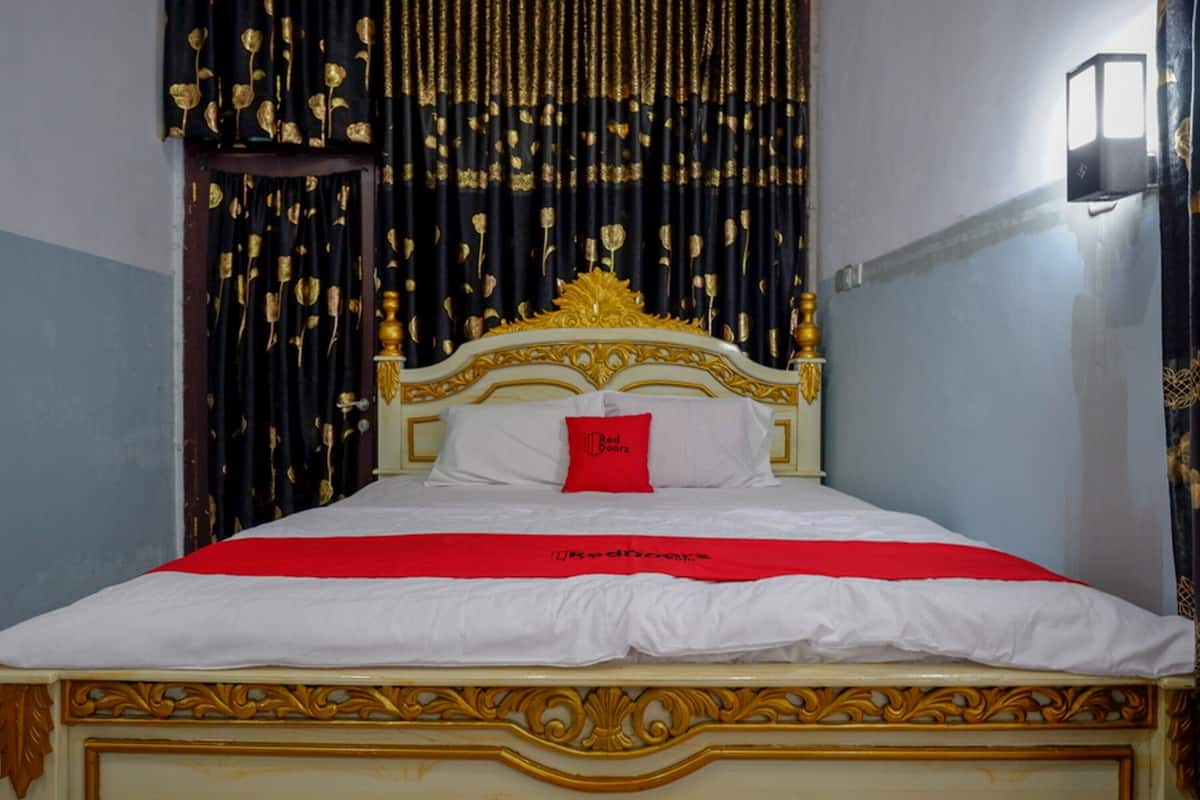 A bed with a white and red bedspread, a red pillow, and a gold headboard.