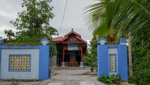 Um edifício tradicional com telhado vermelho e paredes azuis, apresentando uma entrada com azulejos e um pequeno alpendre com cadeiras.