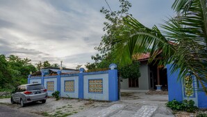 Uma área residencial com uma casa azul, um carro estacionado e uma palmeira.
