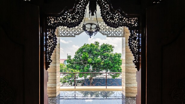 An ornate doorway with a balcony, a metal railing, and a view of a tree and buildings. - RedDoorz Syariah near Exit Toll Banyumanik (Semarang)