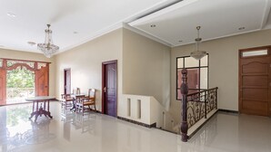A spacious, well-lit hallway with a polished floor, a staircase, and a dining area with wooden furniture. - RedDoorz Syariah near Exit Toll Banyumanik (Semarang)