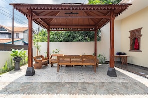 A covered outdoor seating area with a wooden bench and table, surrounded by potted plants and a stone-tiled floor. - RedDoorz Syariah near Exit Toll Banyumanik (Semarang)