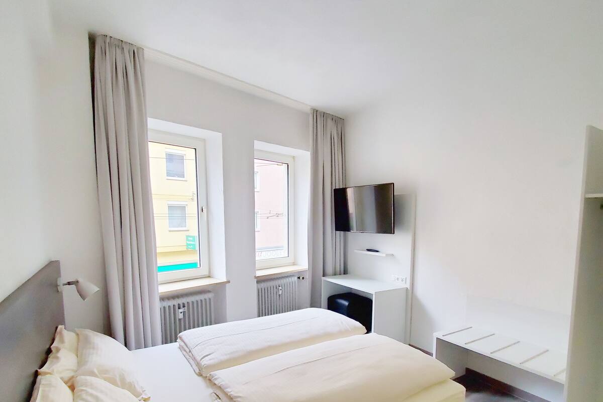 A hotel room with a bed, a desk, a TV, and a window.