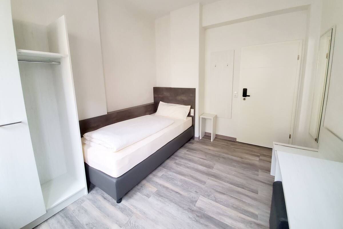 A bedroom with a bed, a small bedside table, and a wardrobe.