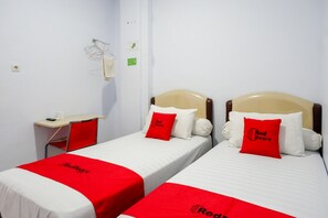 Hotellihuoneessa on kaksi erillistä sänkyä, joissa kummassakin on punainen tyyny ja valkoinen peitto. Huoneessa on myös työpöytä tuolilla sekä pieni pöytä, jonka päällä on kuppi.