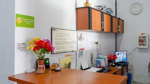 A reception desk with a flower vase, a whiteboard with notes, a clock, and a P3K emergency kit. - RedDoorz @ Hotel Bravo Pantai Kamali Bau Bau (Bau-Bau)