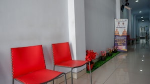 A reception area with two red chairs, a poster, and a small plant arrangement. - RedDoorz @ Hotel Bravo Pantai Kamali Bau Bau (Bau-Bau)