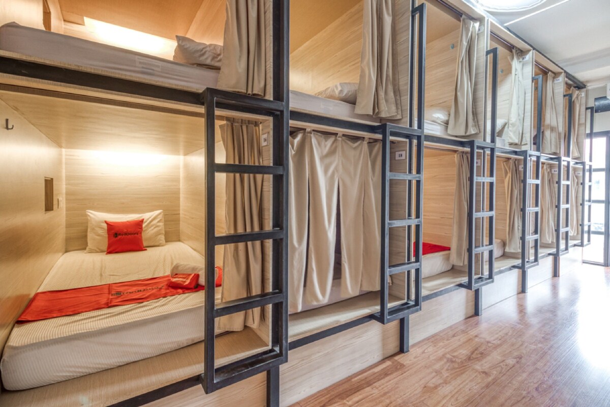A dormitory-style room with bunk beds, wooden flooring, and curtains.