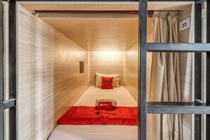 A compact room with a bed, a red blanket, and a pillow with a logo. - RedDoorz Hostel near Stadion Mandala Krida Yogya (Yogyakarta)