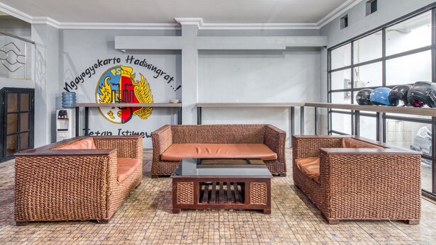 A room with wicker furniture, a table, and a wall with a logo and text. - RedDoorz Hostel near Stadion Mandala Krida Yogya (Yogyakarta)