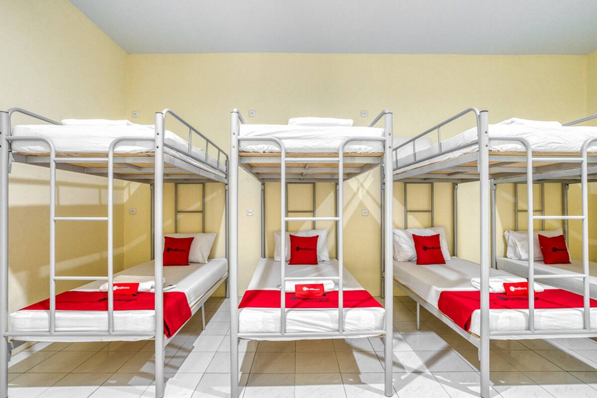 A room with three bunk beds, each with a red pillow and white bedding.