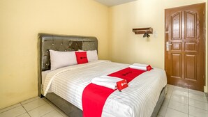 A neatly made bed with a red and white bedspread, a wooden headboard, and a wooden door in the background.