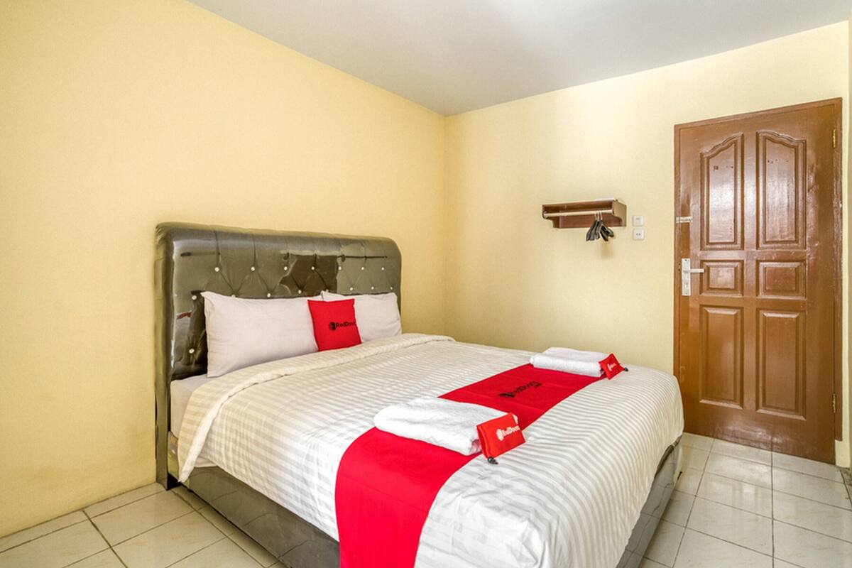 A neatly made bed with a red and white bedspread, a wooden headboard, and a wooden door in the background.