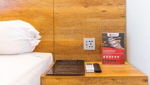 A hotel room with a wooden headboard, a bed with white bedding, a bedside table with a RedDoorz app advertisement, a remote control, and a booklet titled "Selamat Datang MitroTel 1". - RedDoorz Plus near Ringroad City Walks Medan 2 (Medan)