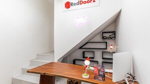 A wooden desk with a computer and a sign that reads "RedDoorz" in a modern interior with a staircase. - RedDoorz Plus near Ringroad City Walks Medan 2 (Medan)