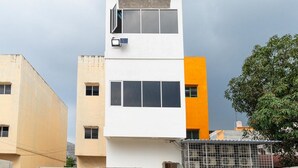 A multi-story building with a white facade, a solar panel, and a tree in the foreground. - RedDoorz Plus near Ringroad City Walks Medan 2 (Medan)