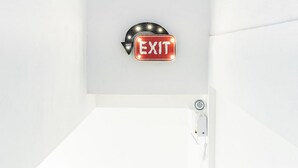 A wall-mounted exit sign with a curved arrow and the word "EXIT" in white letters on a red background. - RedDoorz Plus near Ringroad City Walks Medan 2 (Medan)