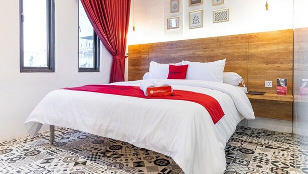 A hotel room with a bed, a red curtain, a wooden headboard, and patterned floor tiles. - RedDoorz Plus near Ringroad City Walks Medan 2 (Medan)