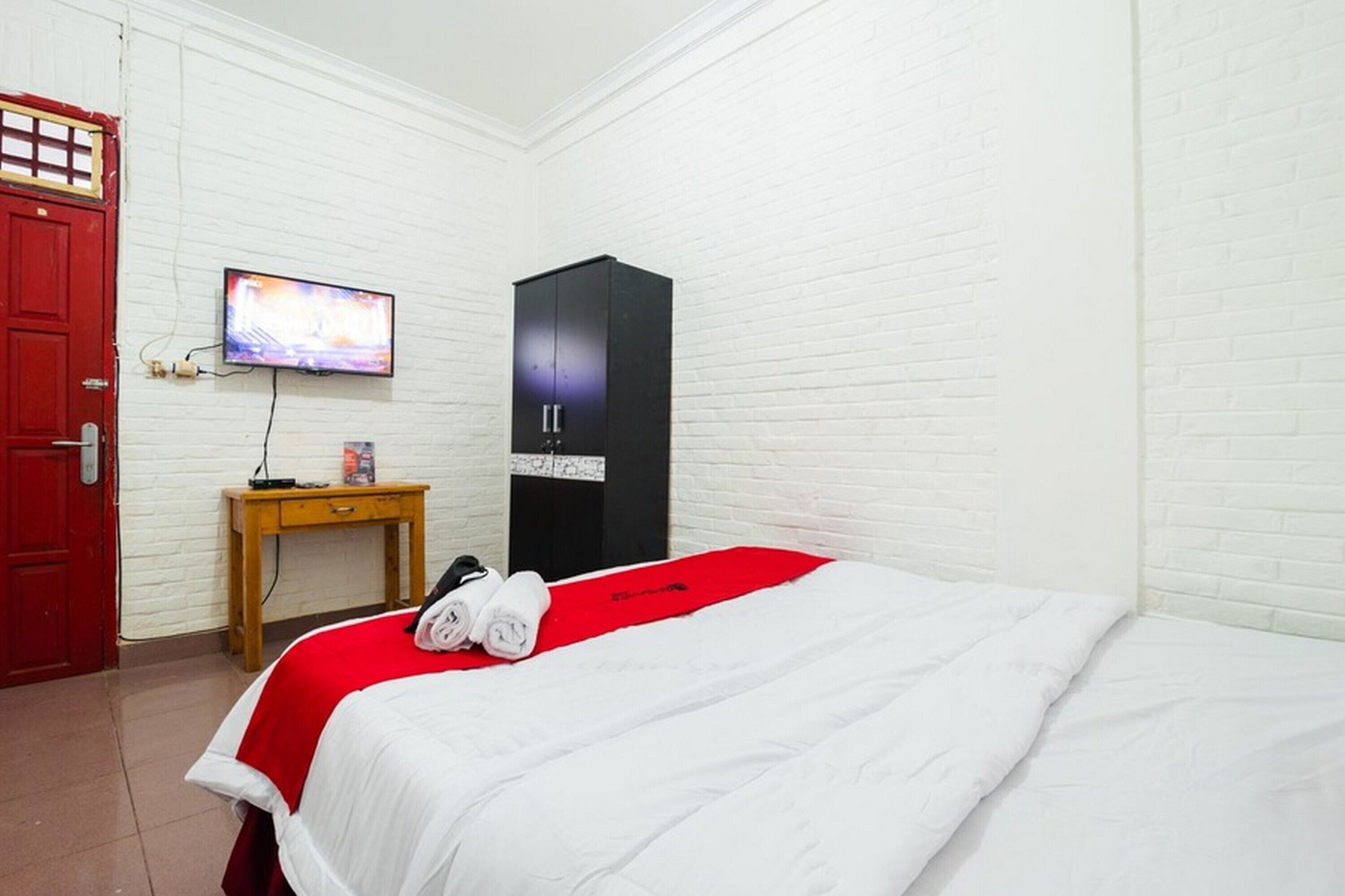 Una habitación de hotel con una cama, un televisor montado en la pared, un escritorio de madera y un armario negro.