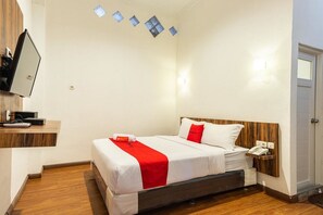 A hotel room with a bed, a bedside table with a phone, a TV mounted on the wall, and a wooden floor. - RedDoorz @ Binjai (Medan)