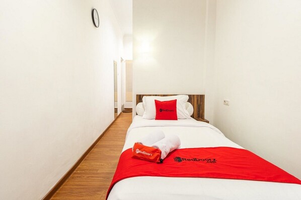 A hotel room with a bed, white walls, wooden flooring, a clock on the wall, and RedDoorz branding on the bedspread and pillows. - RedDoorz @ Binjai (Medan)
