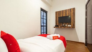 A hotel room with a bed, red pillows, a mounted TV, and a wooden panel wall.
