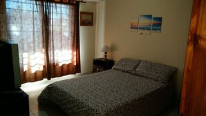 A bedroom with a bed, curtains, a nightstand with a lamp, a painting, and three wall-mounted pictures. - Hermoso Duplex 2 amb. 1 costa  cochera lavarropas,impecable (Mar del Plata)