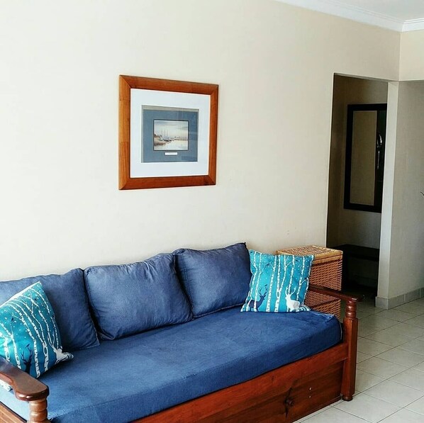 A blue sofa with a wooden frame and a picture frame on the wall.