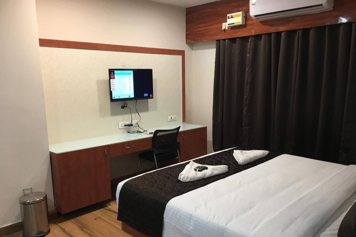 Habitación de hotel con cama, escritorio, computadora y ventana con cortinas.