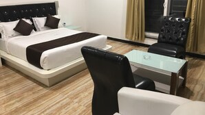 Habitación de hotel con una cama, una mesita de vidrio, una silla y vistas al exterior a través de una ventana con cortinas.