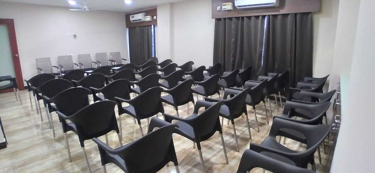 Un salón de conferencias con filas de sillas negras, una pantalla de proyector y un equipo de aire acondicionado en la pared.