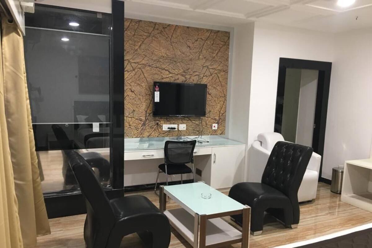 Una habitación moderna con separador de vidrio, un televisor de pantalla plana montado en una pared de mármol, un escritorio con una silla y dos sofás de cuero negro.