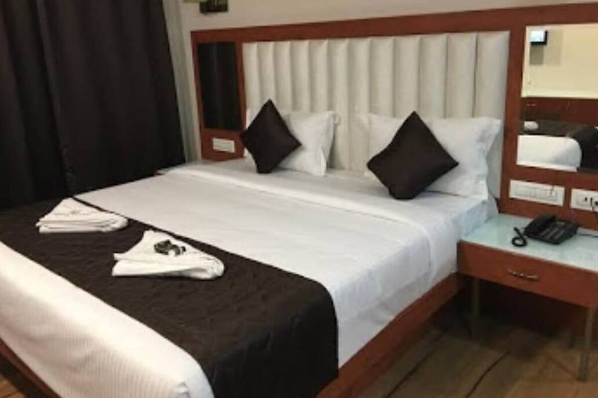 Una habitación de hotel con una cama, una mesita de noche con teléfono y un espejo.