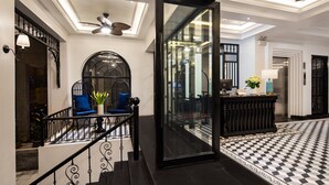 A hotel lobby with a checkered floor, a staircase with black railings, a seating area with blue chairs, and a glass partition. - My Gallery Boutique Hotel & Spa (Sa Pa)