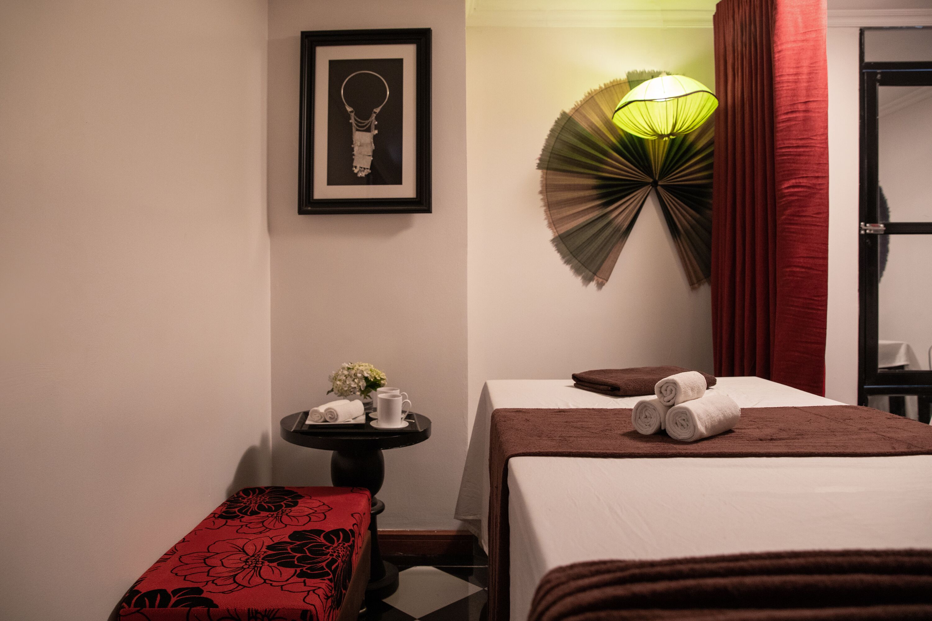 A hotel room with a bed, a small table with a tray of towels, a framed artwork on the wall, and a decorative wall lamp.