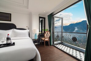 A hotel room with a large bed, a chair, a small table with a bottle and glasses, and a balcony with a mountain view. - My Gallery Boutique Hotel & Spa (Sa Pa)