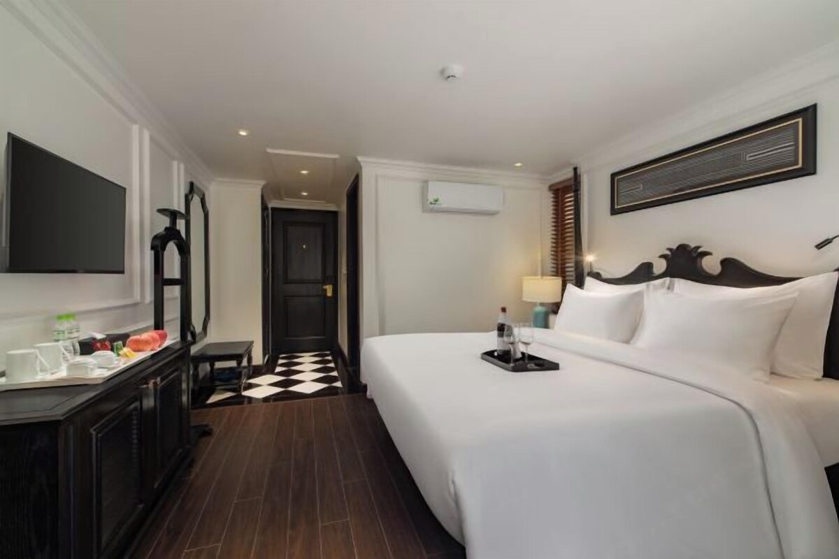 Una habitación de hotel con una cama grande, un televisor de pantalla plana, un escritorio con silla y piso a cuadros.