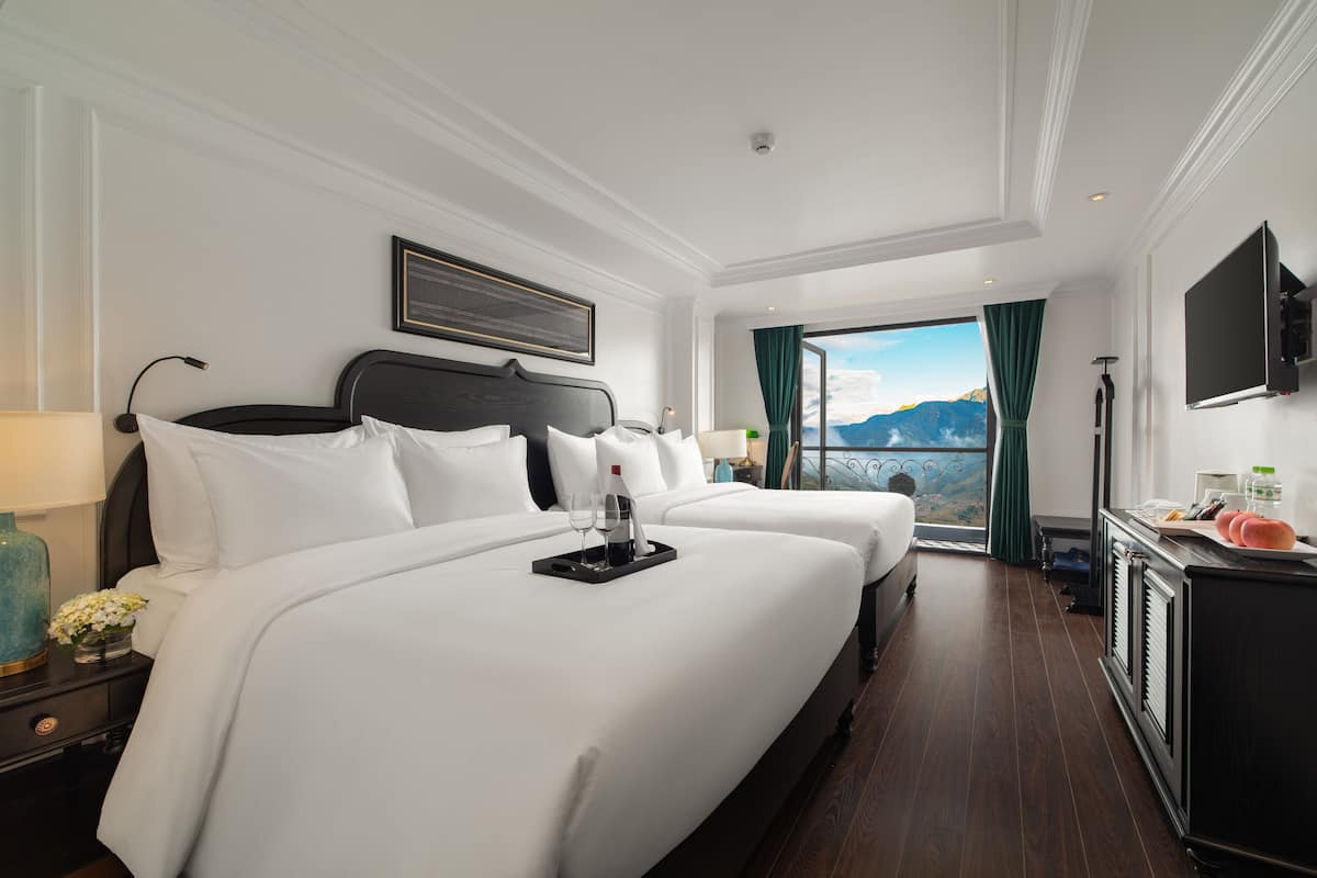 A hotel room with two beds, a TV, and a view of mountains.