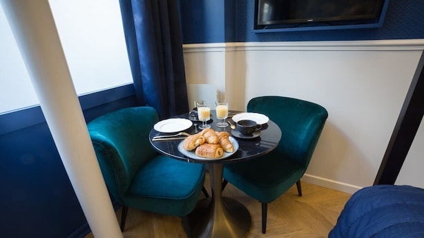 A corner room with teal chairs, a round table with breakfast items, and a TV mounted on the wall. - Le Cafe des Invalides - Eiffel Tower (Paris)