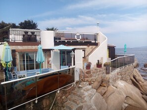 A coastal property with a stone staircase leading to a balcony overlooking the sea. There are outdoor seating areas with umbrellas and a pool. - waterfront villa (Coti-Chiavari)