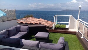 En takterrass med utomhusmöbler, ett räcke och utsikt över havet.