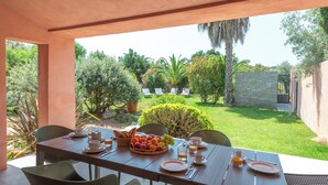 A table set for breakfast with fruits, beverages, and a view of a well-maintained garden and pool area. - GARDEN VILLA 3 MINUTES WALK FROM CALA ROSSA BEACH - RESIDENCE MARINA ROSSA (Lecci)